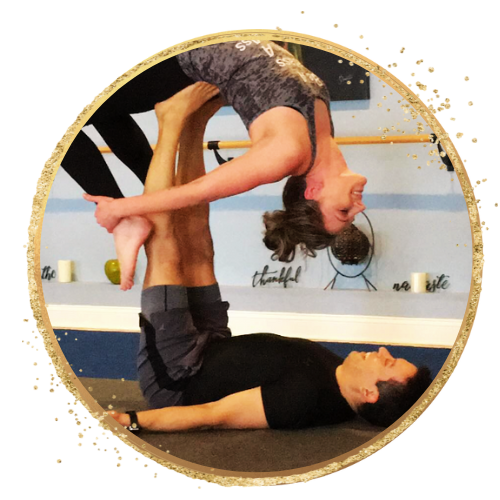 Two people practicing acro yoga, with one person lying on their back supporting the other with their legs.