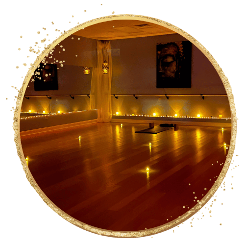 Dimly lit yoga studio with warm lighting and wooden floor, featuring yoga mats and artwork on the walls. Candles line the perimeter, enhancing the serene atmosphere.