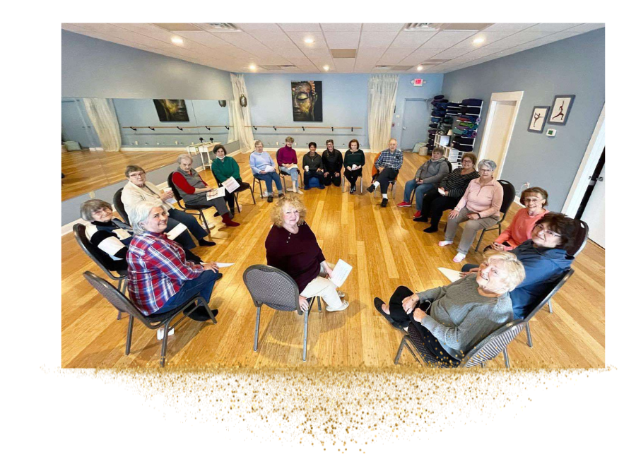 A group of seniors sitting in a circle on chairs in a yoga room with wooden flooring and blue walls.